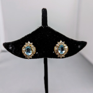 Pode incluir: Um par de brincos de ouro com uma pedra oval azul cercada por pedras brancas menores.