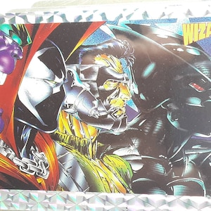 May include: A comic book trading card featuring multiple characters with vibrant colors. The card has a silver, textured border. The word "WIZARD" is displayed in yellow text. The characters include a purple-faced figure, a character with a white mask, and a dark figure.
