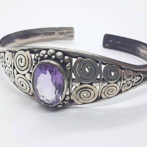 May include: A silver bracelet with a purple amethyst gemstone set in a swirling, ornate design.