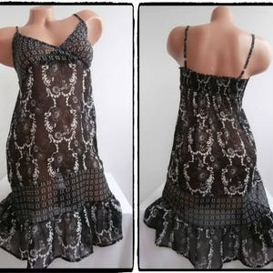 May include: A black and white patterned dress with spaghetti straps. The dress features a V-neckline and a flowing skirt with a ruffled hem. The fabric has a floral design. The dress is displayed on a mannequin.
