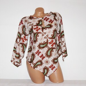 Puede incluir: Una blusa de manga larga con estampado paisley blanco, marrón y verde y escote de ojo de cerradura.