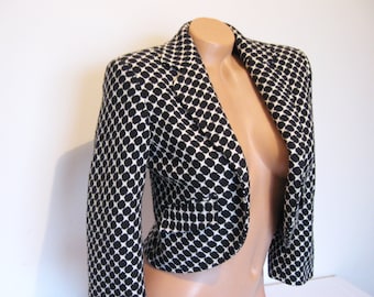 May include: A black and white cropped blazer with a geometric pattern. The blazer has a notched collar and long sleeves.