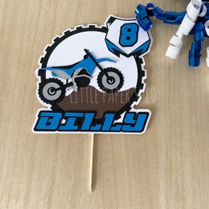 May include: A blue and white cake topper with a dirt bike, the number 8, and the name "BILLY".