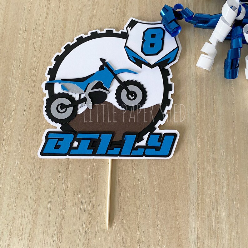 May include: A blue and white cake topper with a dirt bike, the number 8, and the name "BILLY".