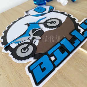 May include: Blue and black motocross cake topper with a dirt bike and the word "Bike" in large blue letters.