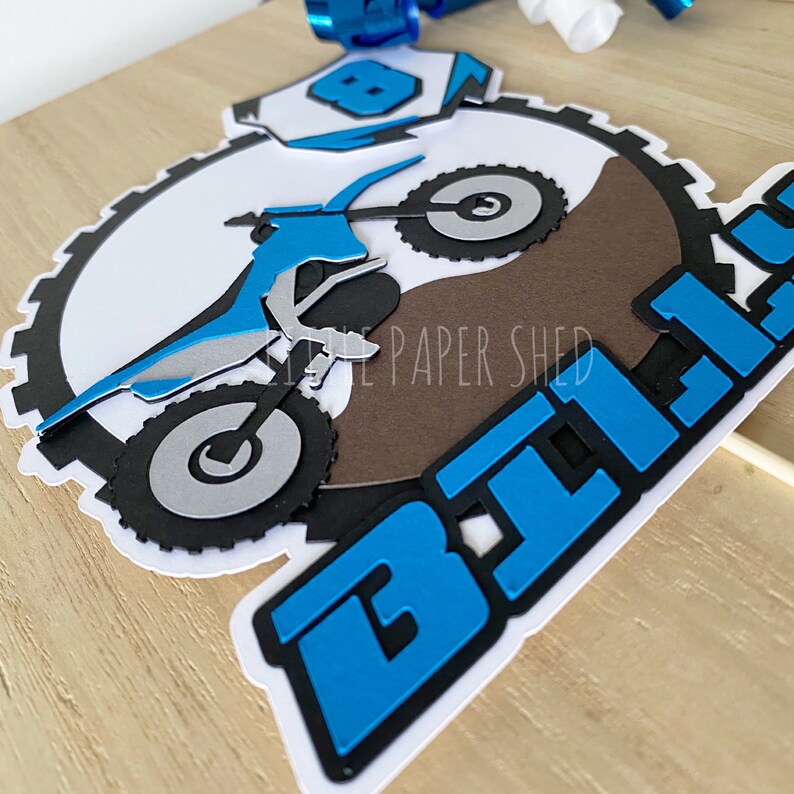 May include: Blue and black motocross cake topper with a dirt bike and the word "Bike" in large blue letters.