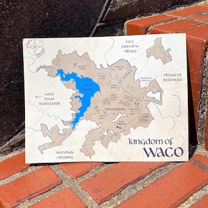 May include: A rectangular map of Waco, Texas, with a blue Waco Lagoon and surrounding areas in brown. The map includes text such as "Kingdom of Waco," "Town Square," and "West Texas Wastelands." The map is displayed on a brick surface.