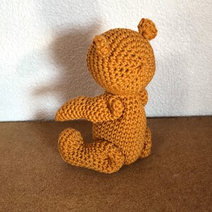 May include: A crocheted stuffed animal in the shape of a small dragon. The dragon is sitting on its hind legs with its wings spread out. It is made of a soft, mustard yellow yarn.
