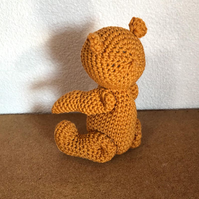 May include: A crocheted stuffed animal in the shape of a small dragon. The dragon is sitting on its hind legs with its wings spread out. It is made of a soft, mustard yellow yarn.