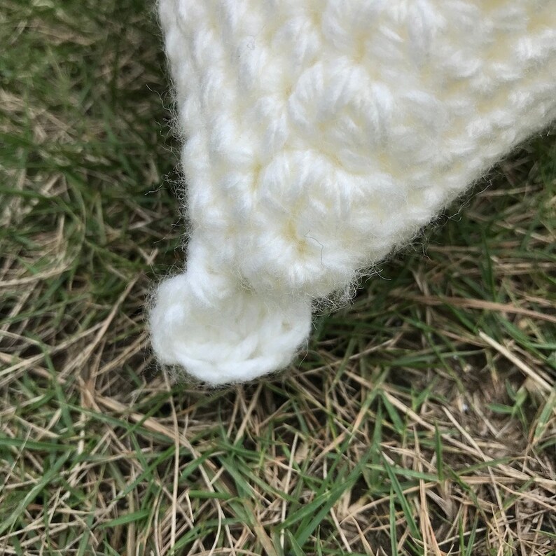 May include: Close-up of a white crocheted hat with a textured design. The hat has a small, round pom-pom on top.