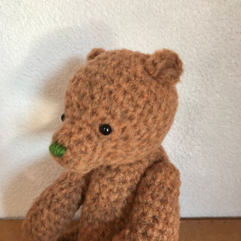 May include: A brown crocheted teddy bear with black eyes and a green nose.
