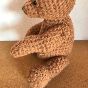 May include: A brown crocheted teddy bear with black eyes and a green nose.