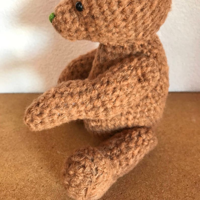 May include: A brown crocheted teddy bear with black eyes and a green nose.