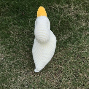 May include: A white crocheted swan with a yellow beak. The swan is sitting on a bed of green grass.