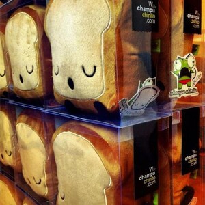 Puede incluir: Juguetes de peluche con forma de rebanadas de pan con caras sonrientes se exhiben en cajas de pl&aacute;stico transparente. El pan tiene un centro de color beige claro y una corteza marr&oacute;n oscuro. El texto "W. champu chinito .com" es visible.