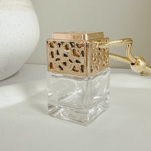 May include: A gold car air freshener with a clear glass bottle and a decorative gold top. The top has a textured design with small circles and ovals.