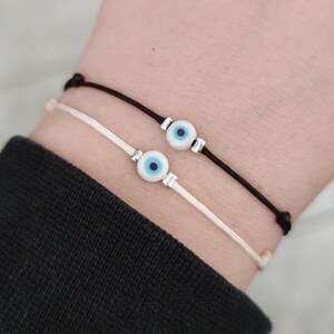 May include: Two bracelets with black and white string and a blue evil eye charm on each.