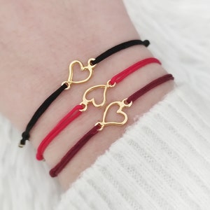 Puede incluir: Tres pulseras de la amistad con dijes de corazón de oro. Las pulseras son rojas, negras y burdeos.
