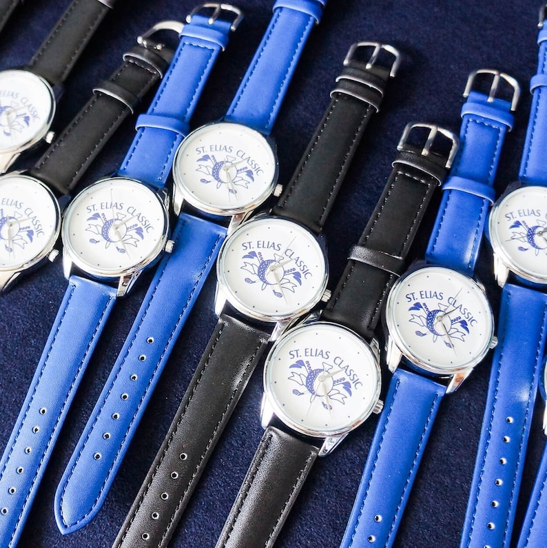 May include: A group of seven wristwatches with blue and black leather bands. The watch faces are white with black lettering that reads "ST. ELIAS CLASSIC".