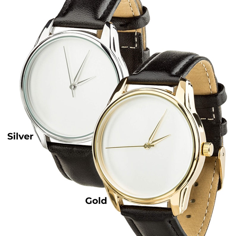 May include: Two wristwatches with black leather bands. The watch on the left has a silver case and the watch on the right has a gold case. Both watches have white faces with black hands.