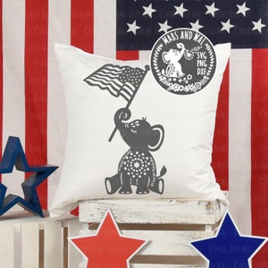 Puede incluir: Una almohada blanca con una silueta gris de un elefante sosteniendo una bandera estadounidense. El elefante está decorado con un círculo de estrellas. La almohada está sentada en una caja de madera con estrellas rojas, blancas y azules en los lados. El texto "Mars and Wal" está en un círculo con una corona alrededor. El texto "SVG PNG DXF" está debajo del círculo.