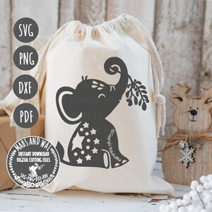 Puede incluir: Una bolsa de lona blanca con una silueta negra de un elefante sosteniendo una rama de muérdago. El elefante está decorado con estrellas blancas. La bolsa tiene un cierre de cordón y es perfecta para regalar.