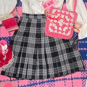 Puede incluir: Una blusa blanca con cuello de volantes y mangas largas, una falda de cuadros negros y blancos, un bolso de crochet rosa en forma de corazón con una correa blanca y un cartel rosa que dice "Be Mine".