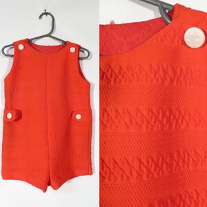 May include: Red sleeveless jumpsuit with white buttons and pockets. The fabric has a textured pattern.