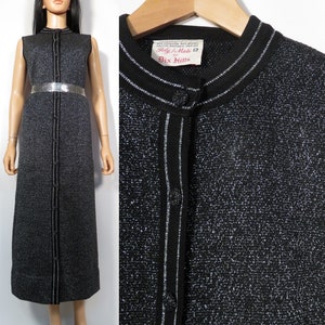 Op de afbeelding: Een mouwloze zwarte en zilveren glinsterende jurk met een knoopsluiting aan de voorkant en een zilveren rand. De jurk heeft een label met de tekst "Poly-Mate 12 by Dix Arts".