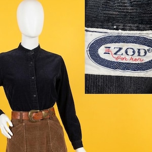 May include: A black long-sleeve corduroy button-down shirt with a mandarin collar and a brown plaid corduroy skirt featuring two front pockets and a brown leather belt. The shirt label reads IZOD for her in blue and red text on a white background.