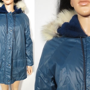 May include: A teal winter coat featuring a hood with faux fur trim and a dark blue lining. The coat has a button-up front, two front pockets, and a drawstring hood. The coat is displayed on a mannequin.
