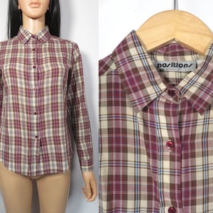 May include: A long-sleeved plaid shirt with a button-down collar. The shirt is brown, beige, and burgundy with a blue plaid pattern. The shirt has a label that says "positions" on it.