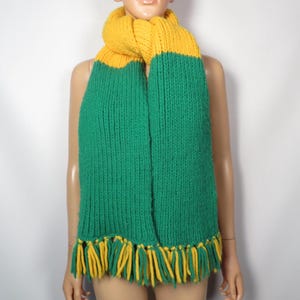 May include: A green and yellow knitted scarf with fringe. The scarf is made of a soft, chunky yarn and has a simple, classic design.