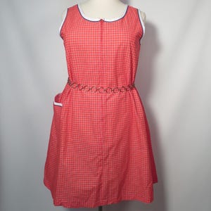 May include: A vintage red and white checkered dress with a white and blue trim neckline and a metal chain belt. The sleeveless dress has a zipper down the front and a small pocket on the side. The dress is displayed on a mannequin.