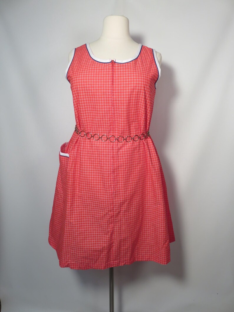 May include: A vintage red and white checkered dress with a white and blue trim neckline and a metal chain belt. The sleeveless dress has a zipper down the front and a small pocket on the side. The dress is displayed on a mannequin.