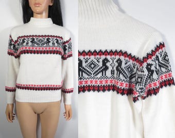 May include: A cream-colored turtleneck sweater with a geometric pattern in black and red. The pattern includes stylized bird figures and diamond shapes. The sweater has long sleeves and a ribbed hem and cuffs.