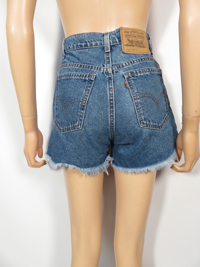以下が含まれることがあります： フリンジヘムのブルーデニムのショートパンツ。ショートパンツの後ろには、"Levi Strauss & Co.  Quality Clothing"と"37501"の文字が書かれた茶色の革のパッチが付いています。