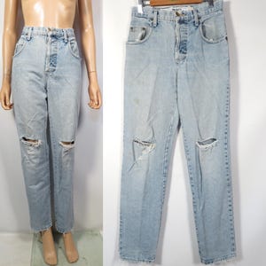 May include: Light blue denim jeans with distressed knee holes. The jeans have a high waist and a straight leg fit.