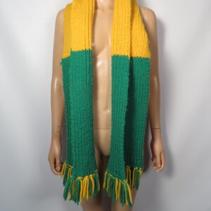 May include: A yellow and green knitted scarf with fringe tassels. The scarf is made of a soft, chunky yarn.