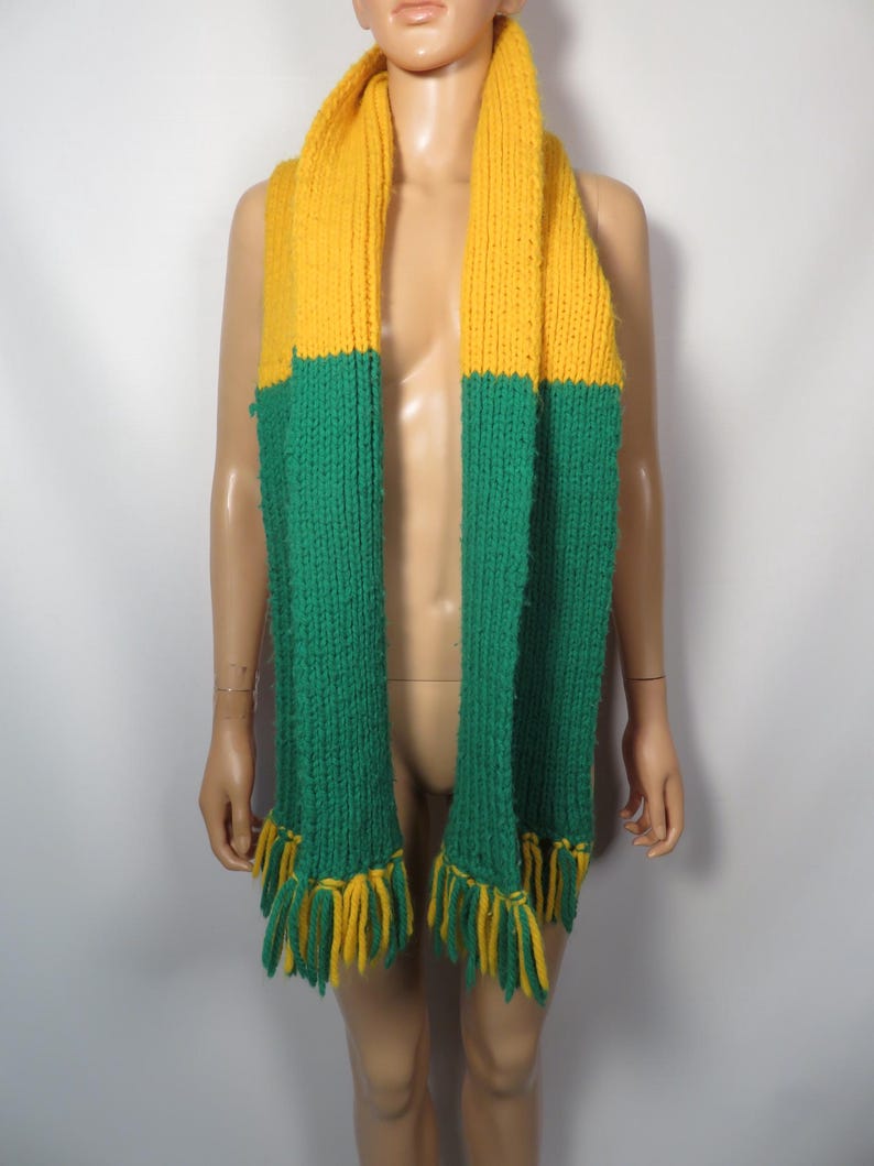 May include: A yellow and green knitted scarf with fringe tassels. The scarf is made of a soft, chunky yarn.