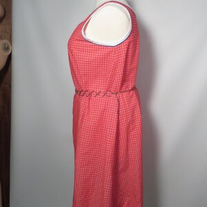 May include: A red plaid sleeveless dress with white and blue trim around the neckline. The dress has a matching chain belt. The dress is displayed on a mannequin.