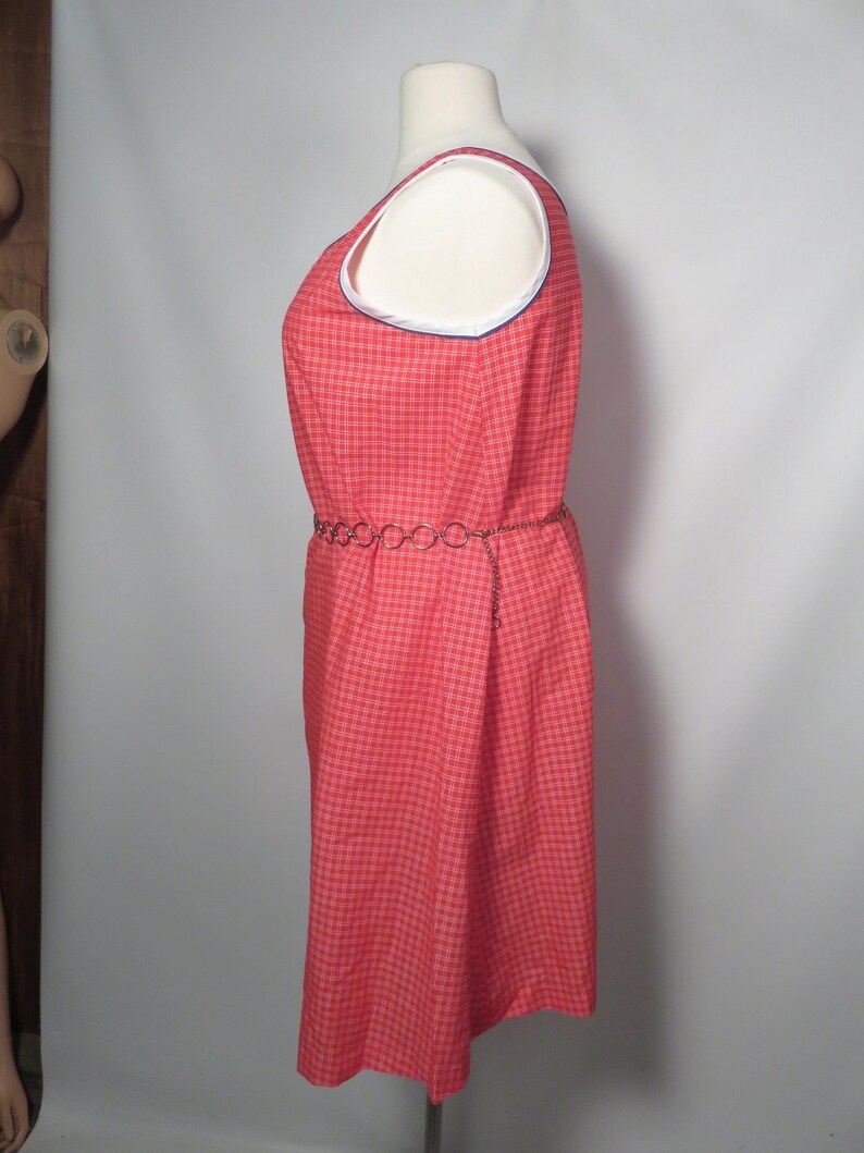 May include: A red plaid sleeveless dress with white and blue trim around the neckline. The dress has a matching chain belt. The dress is displayed on a mannequin.