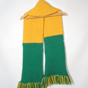 May include: A yellow and green knitted scarf with fringe on the ends. The scarf is hanging on a wooden hanger.