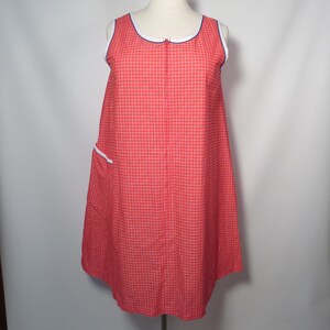 May include: A sleeveless red and white checkered dress with a white and blue trim around the neckline and armholes. The dress has a zipper down the front and a pocket with white trim. The dress is displayed on a mannequin.