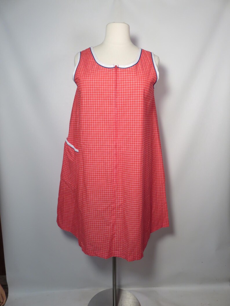 May include: A sleeveless red and white checkered dress with a white and blue trim around the neckline and armholes. The dress has a zipper down the front and a pocket with white trim. The dress is displayed on a mannequin.