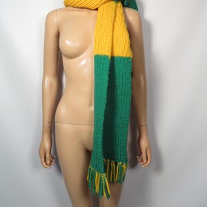 May include: A long knitted scarf with a yellow and green color block design. The scarf has fringe on the ends.