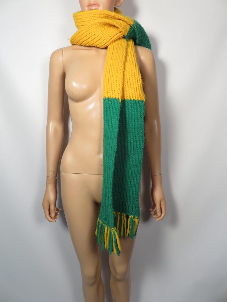 May include: A long knitted scarf with a yellow and green color block design. The scarf has fringe on the ends.