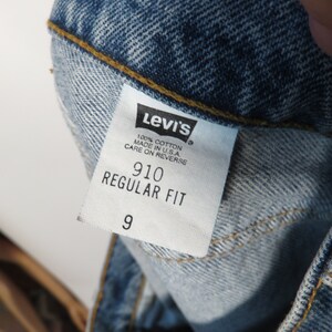 以下が含まれることがあります： 「Levi's」という文字、 「100% コットン」、「米国製」、「裏返してのお手入れ」、「910 レギュラーフィット」、「9」という文字が書かれた白い Levi's タグ。