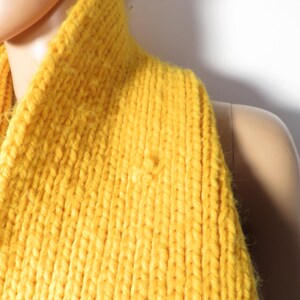 May include: A close-up of a yellow knitted turtleneck sweater. The sweater is made of a soft, chunky yarn and has a ribbed texture.