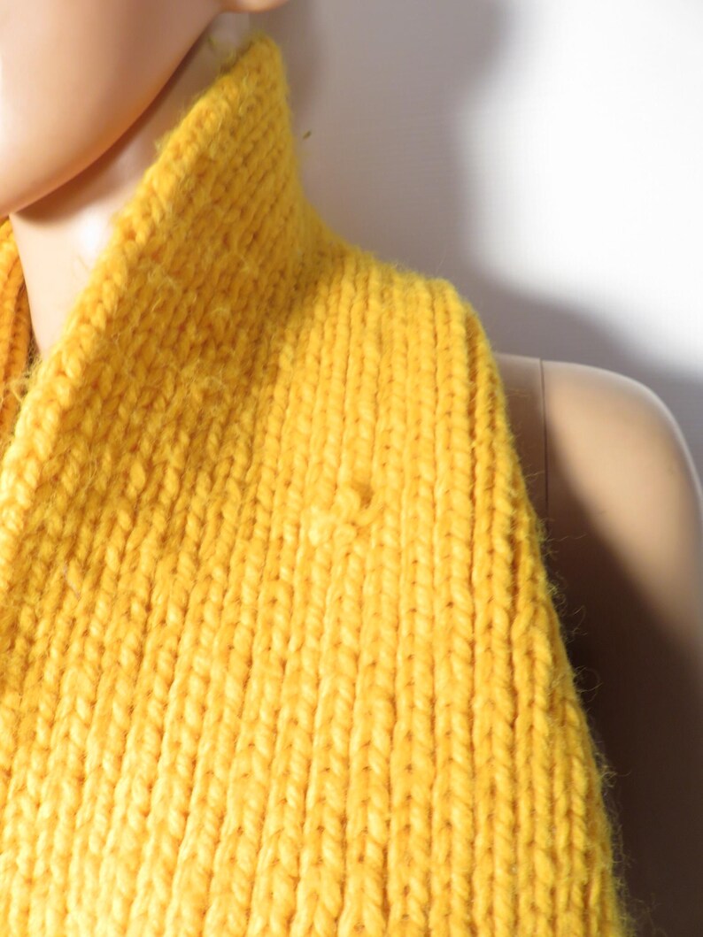 May include: A close-up of a yellow knitted turtleneck sweater. The sweater is made of a soft, chunky yarn and has a ribbed texture.